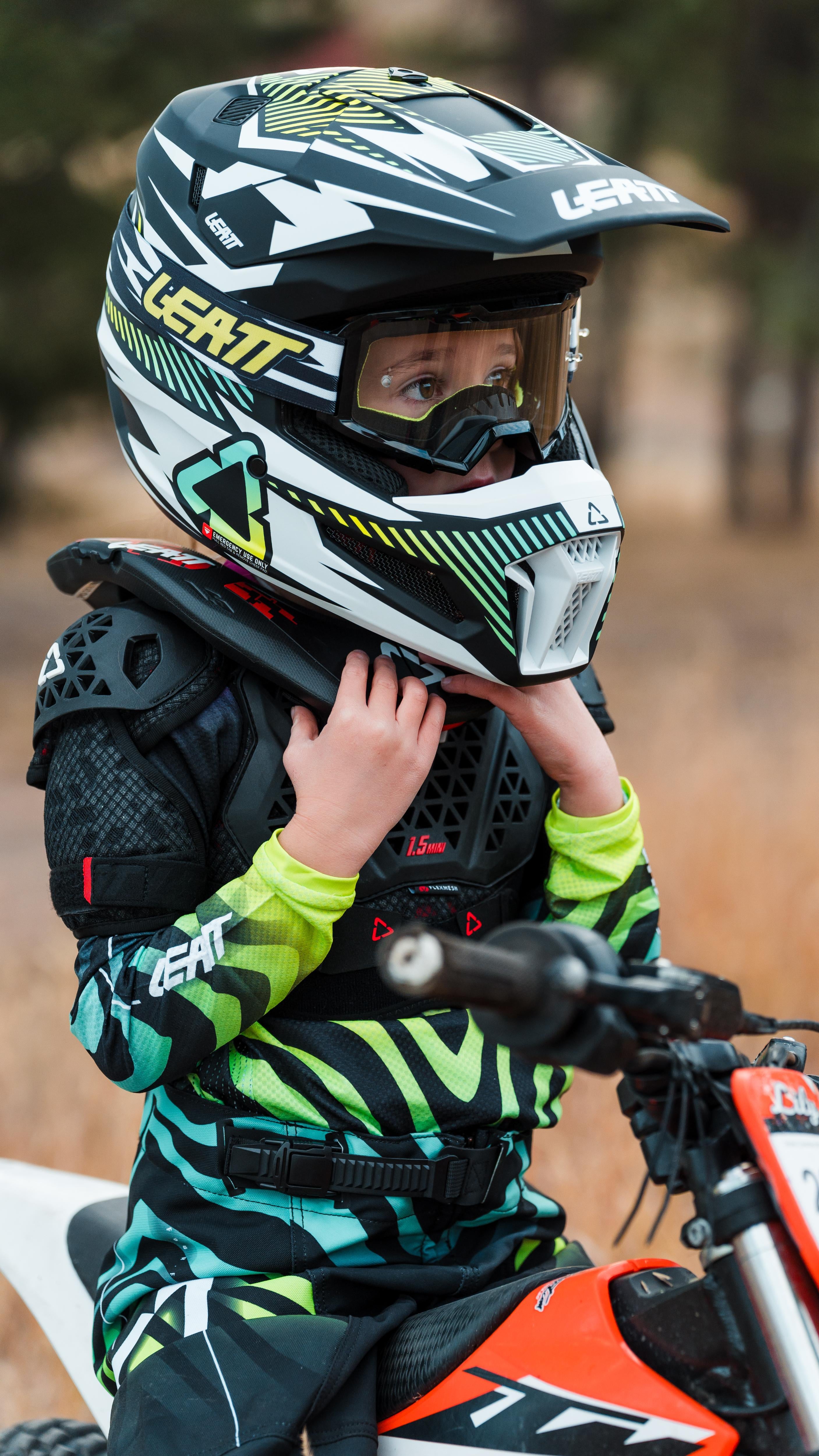 Child wearing a motocross helmet and protective gear on a dirt bike.
