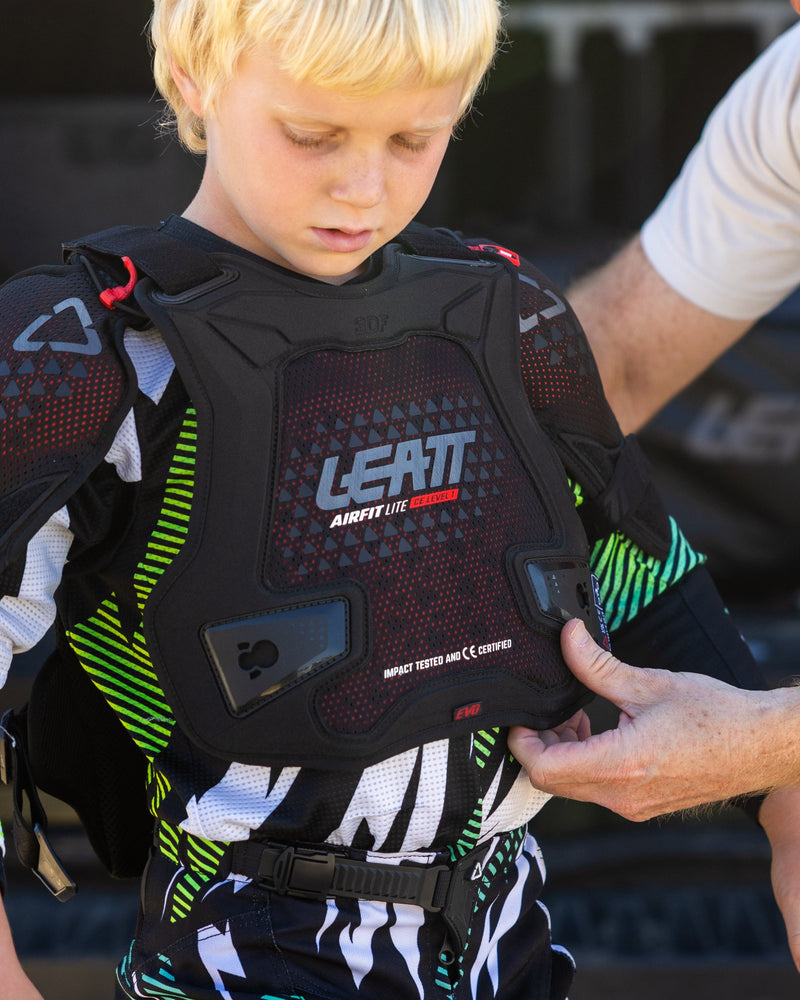 Child wearing motocross gear with a parent adjusting the gear in an outdoor setting.