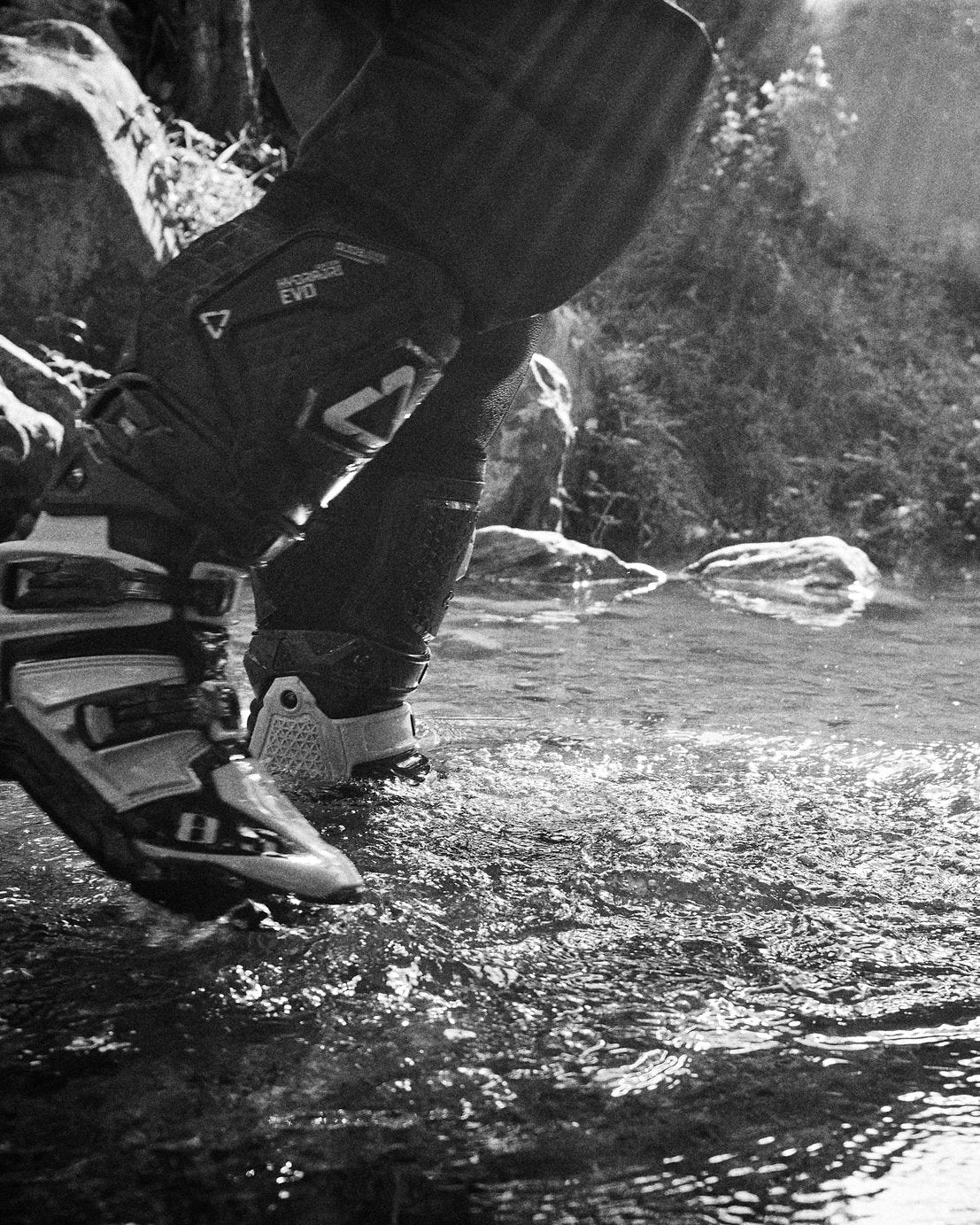 Person stepping into water with a backpack, surrounded by nature