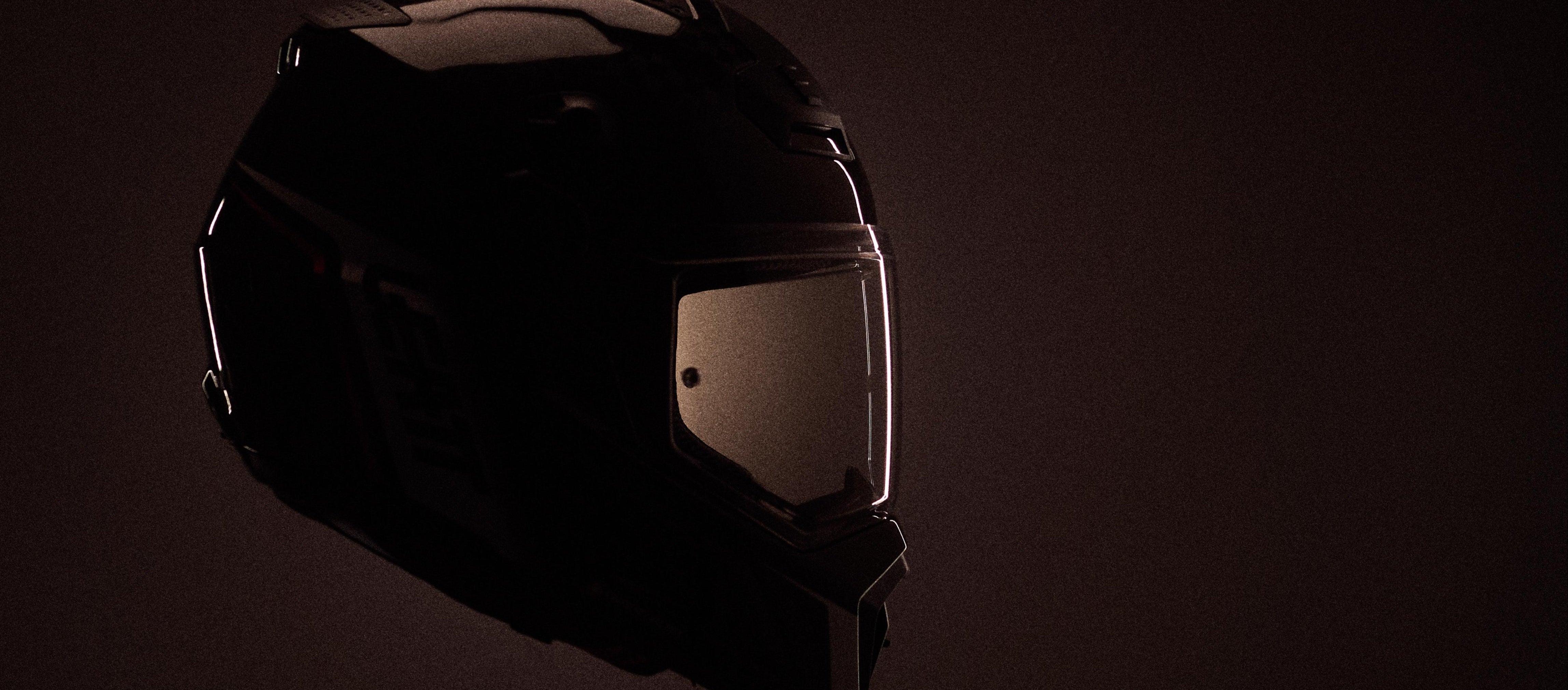 A dark full-face motorcycle helmet with a tinted visor, shown in dramatic low light against a dark brown background.