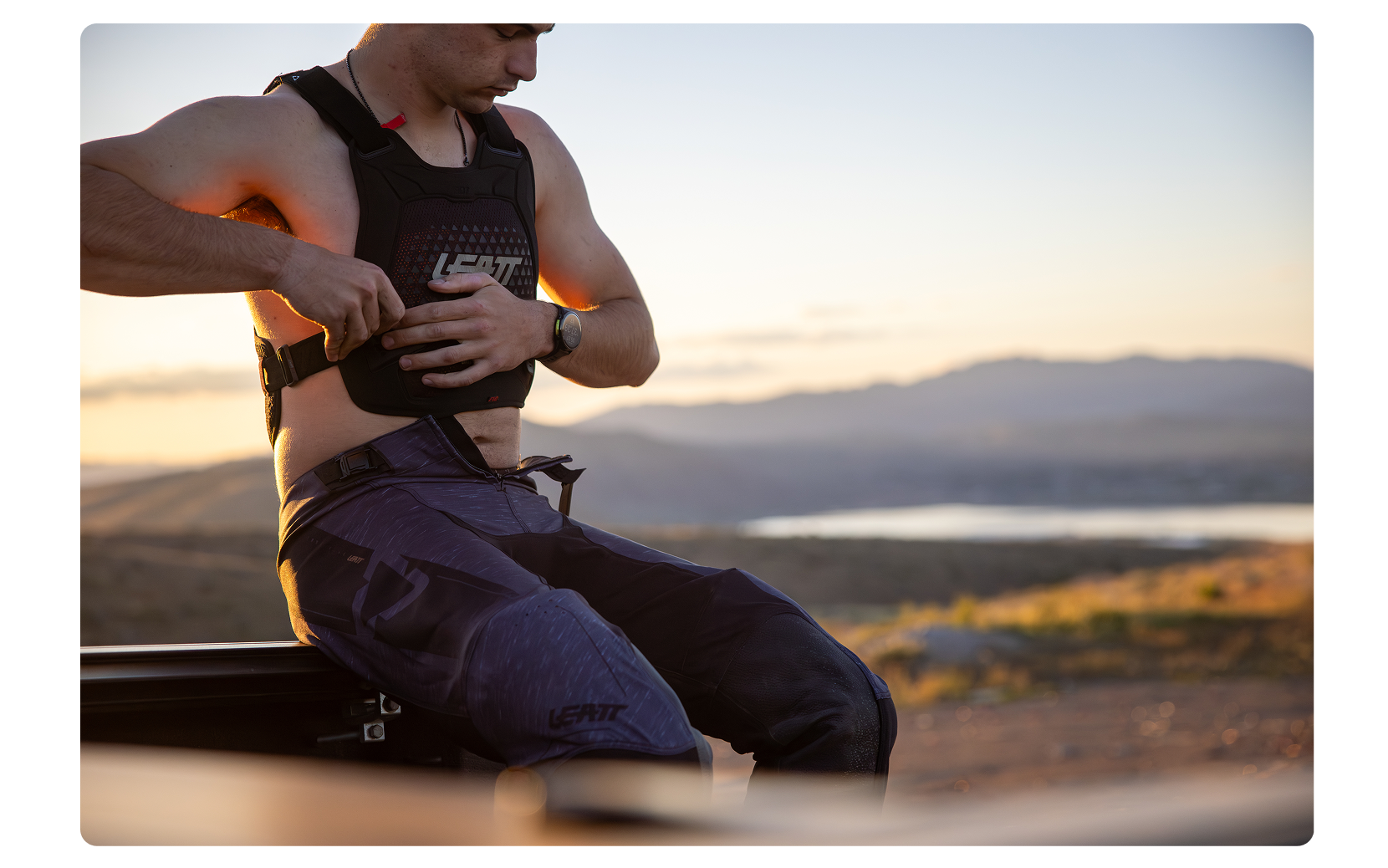 Person adjusting a chest protector in a desert landscape during sunset