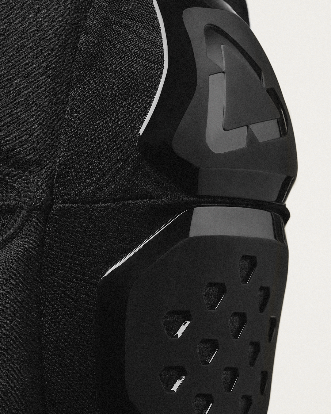 Close-up of black protective knee armor with a textured fabric sleeve and a white accent line, shown against a light gray background.