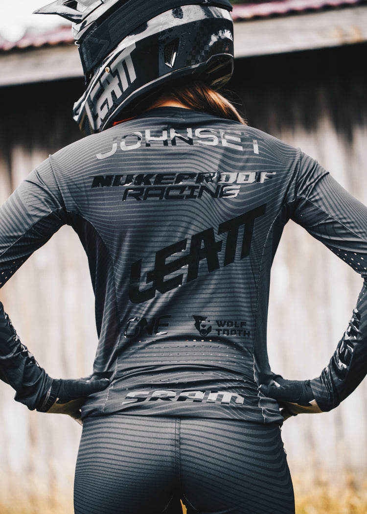 Person wearing a gray racing suit with visible branding in an outdoor setting