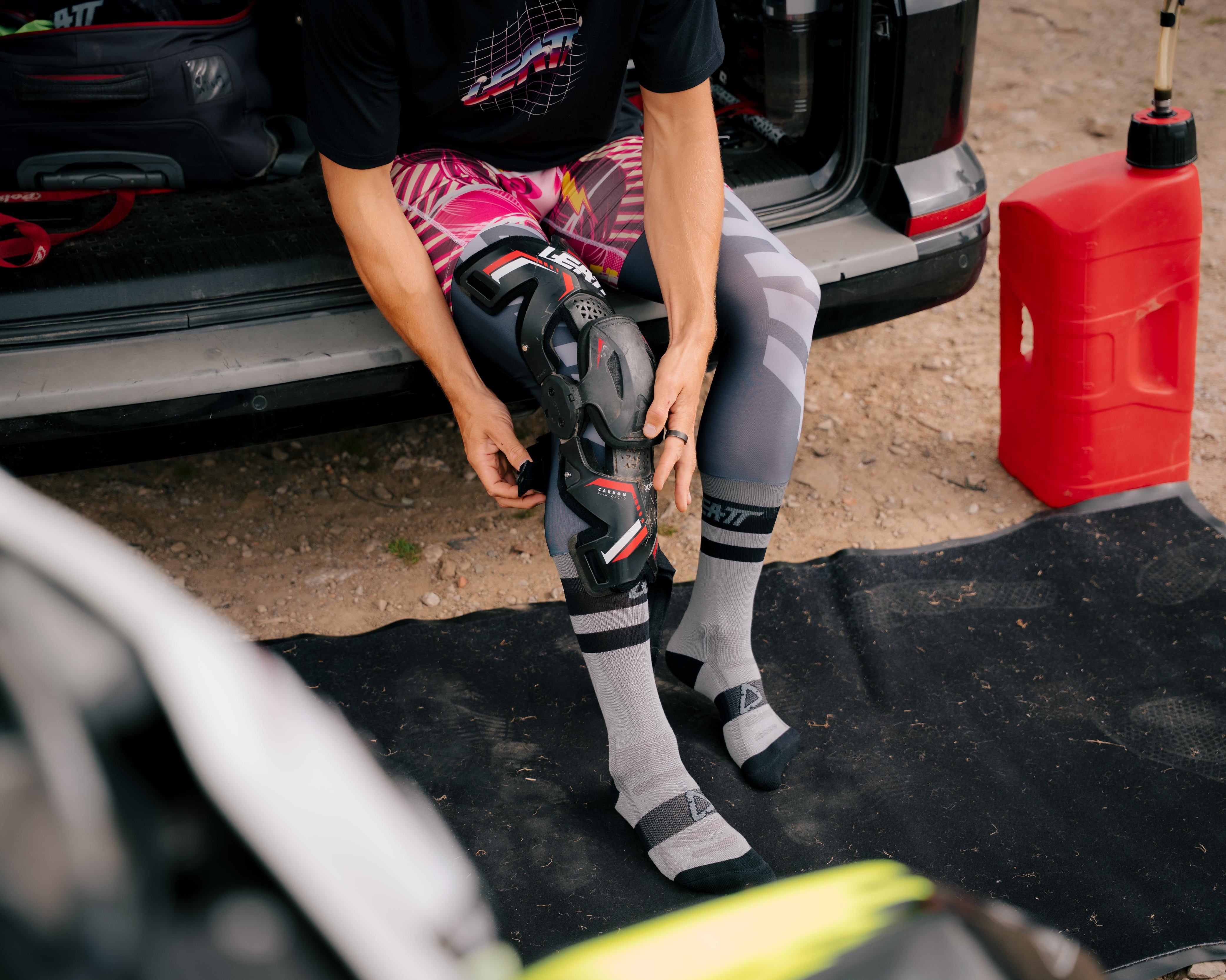 Person adjusting motorcycle boots near an open vehicle trunk with a red fuel container.
