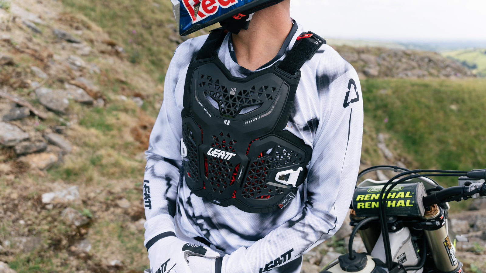 Person wearing a motocross outfit with a Leatt chest protector on a bike in a natural setting.