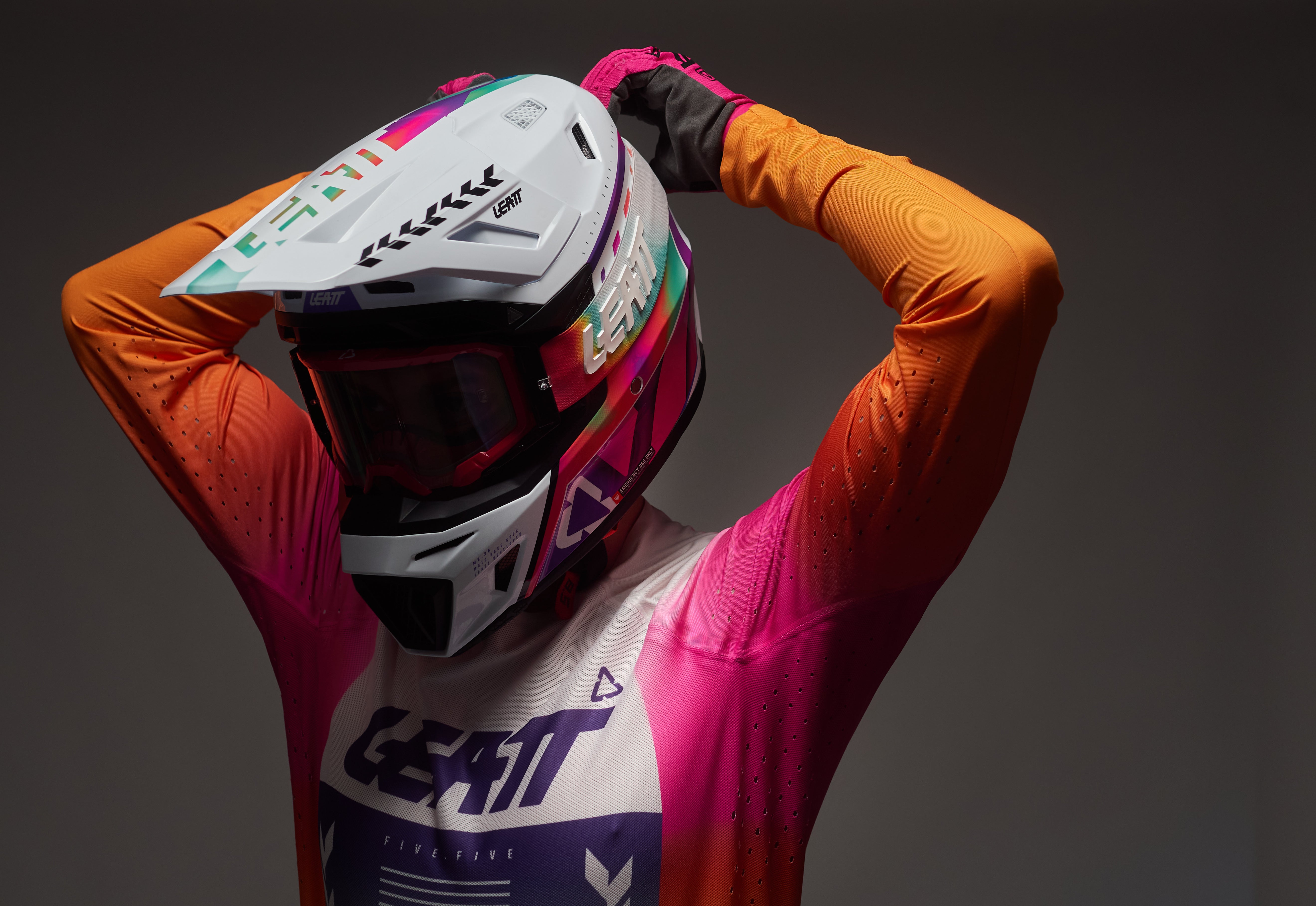 Person wearing a colorful motocross helmet and outfit with 'Leatt' branding on a dark background