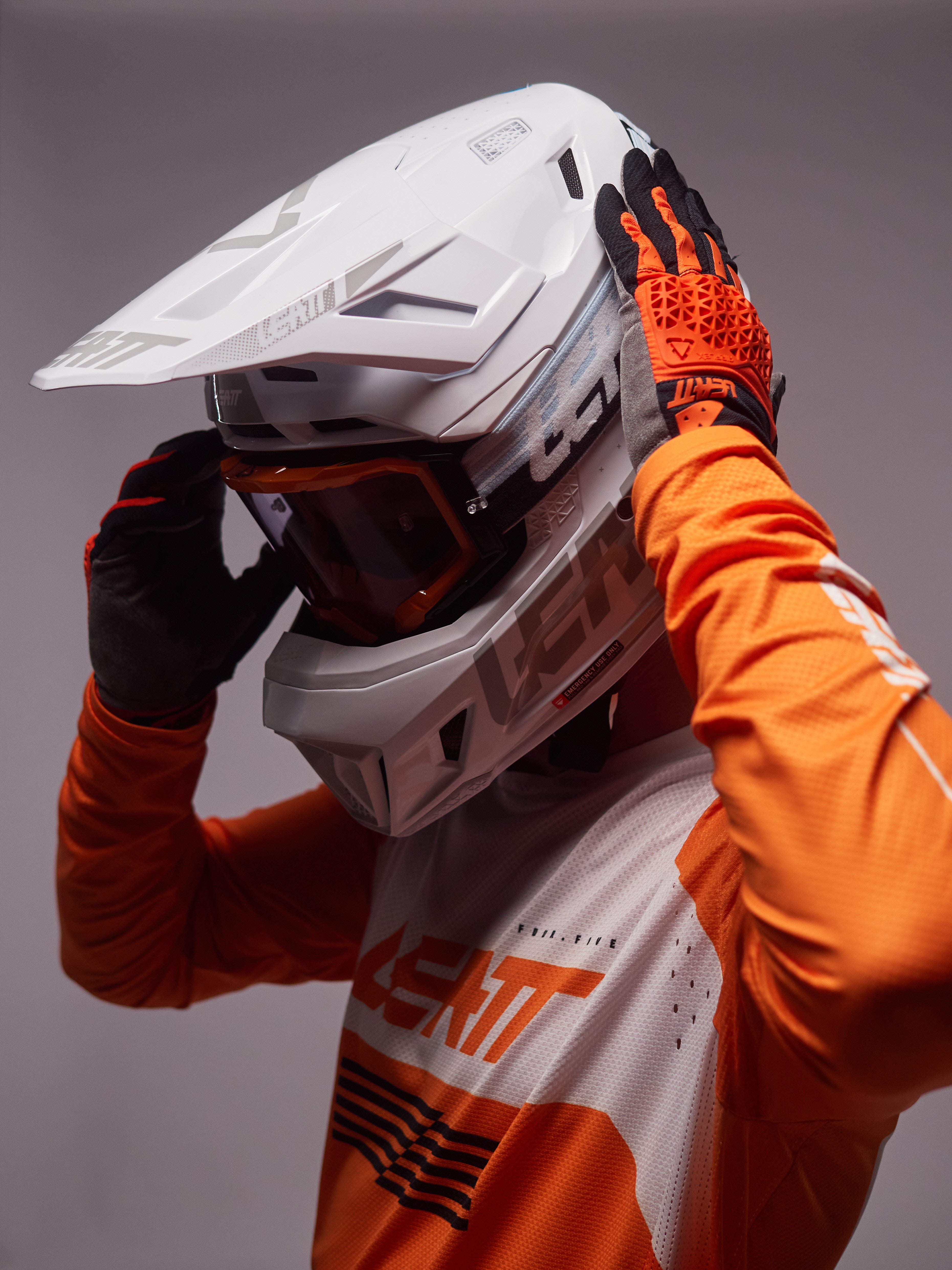 Person wearing an orange and white motocross helmet and outfit against a gray background