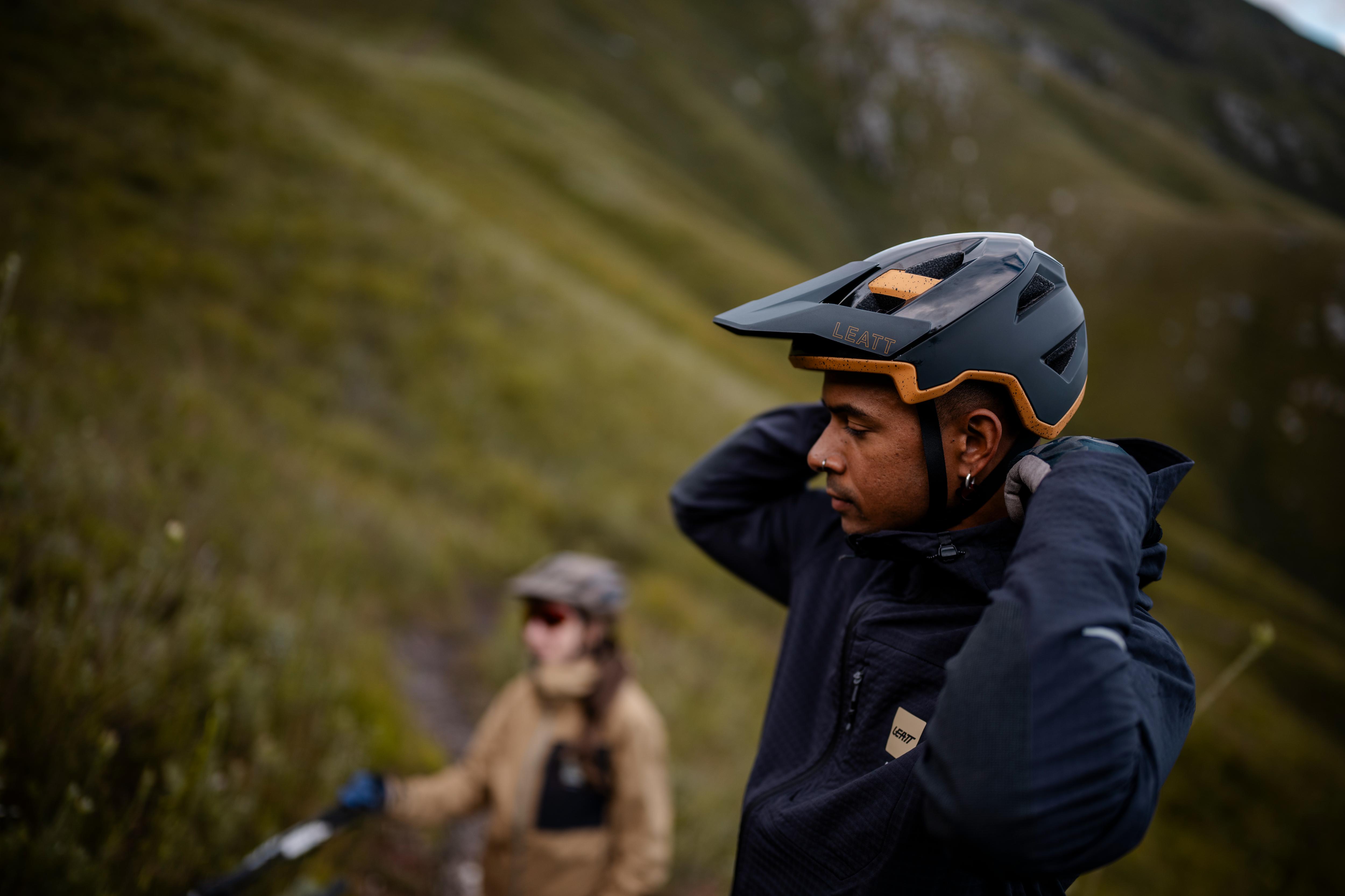 Two people in mountain biking gear on a trail with mountains in the background