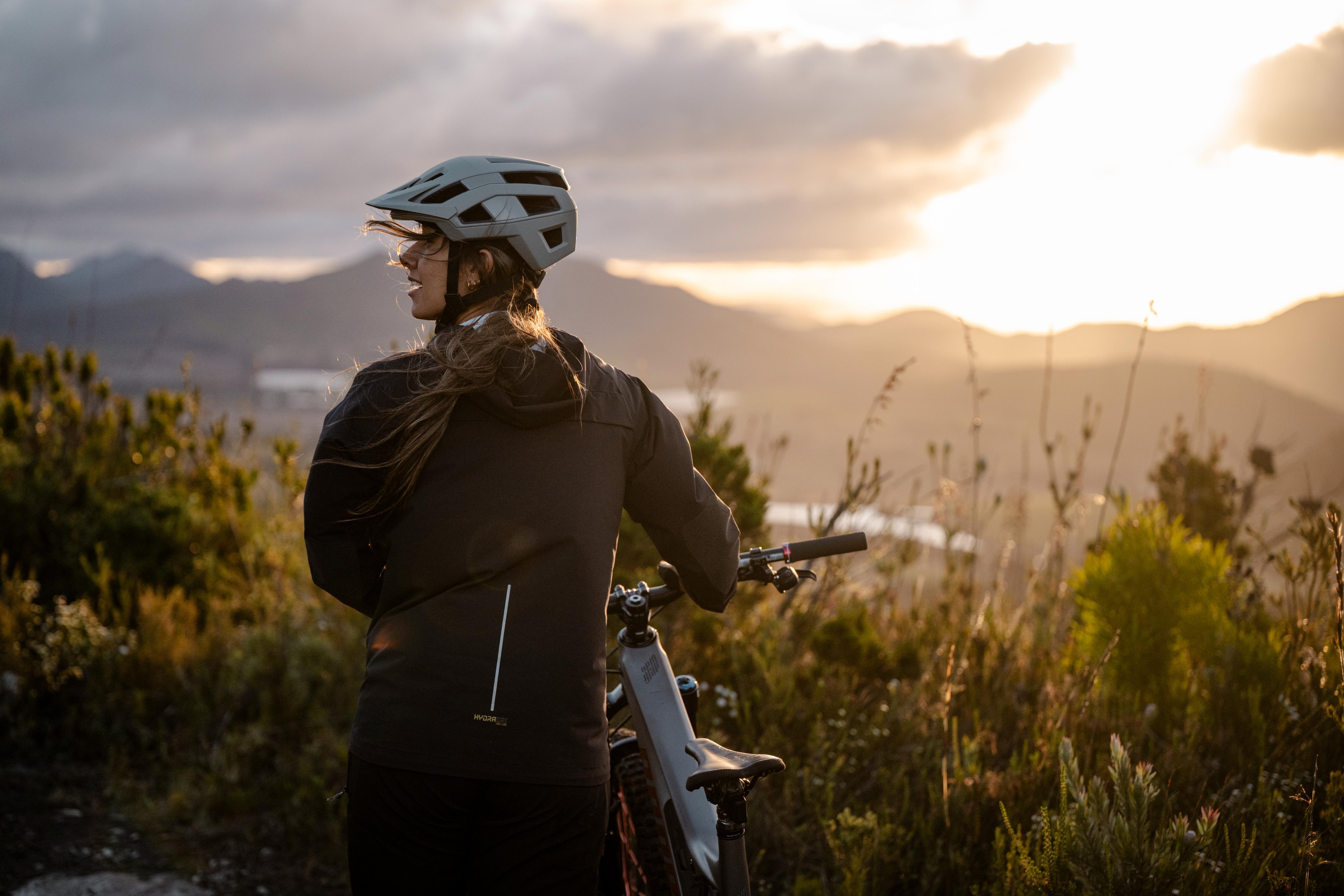 Person with a bicycle standing in a field with mountains in the background