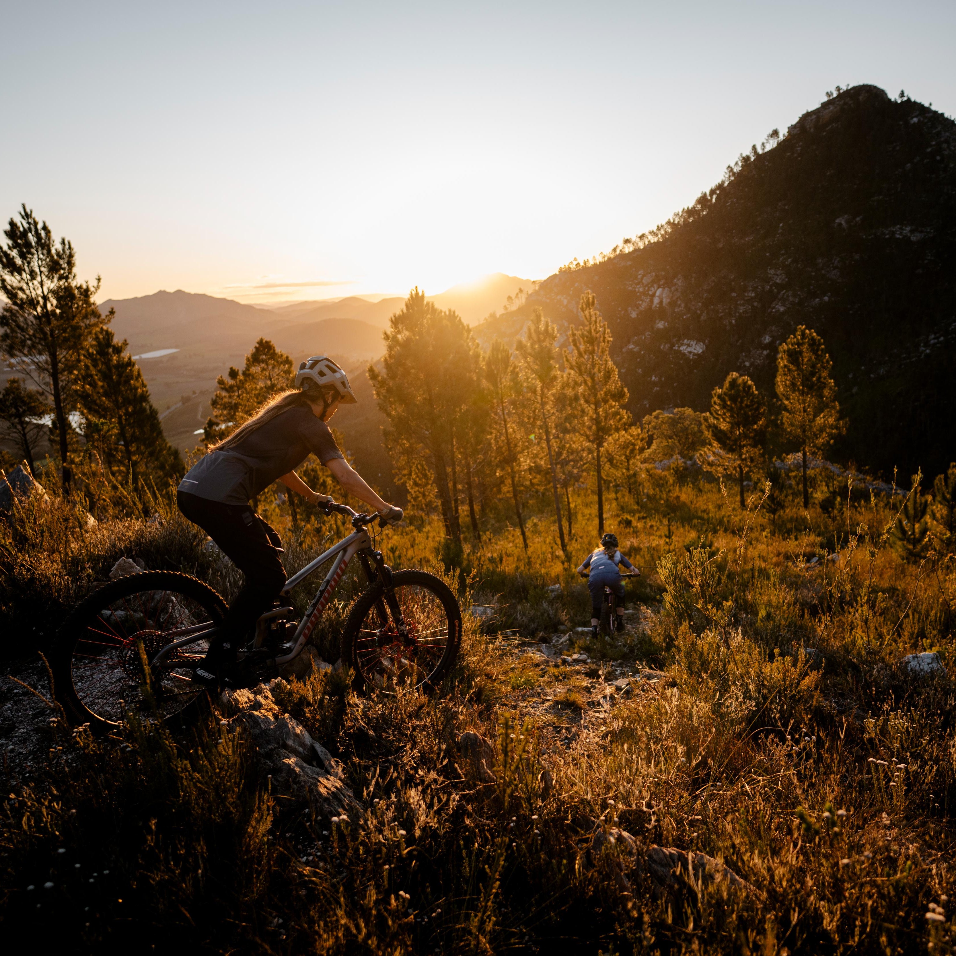 Two mountain bikers riding on a trail with a sunset in the background